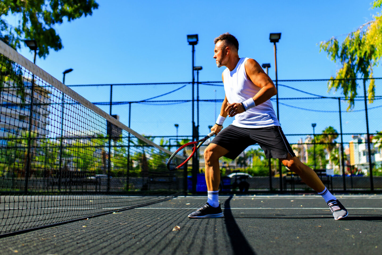 Mature handsome man playing tennis on tennis court at sunny day